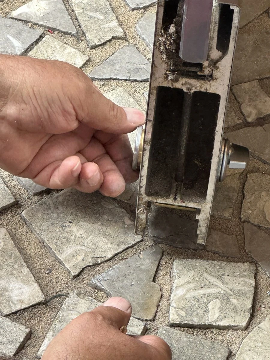 Locksmith hand next to a worn mortise lock body pulled from a commercial door, set on a stone sidewalk