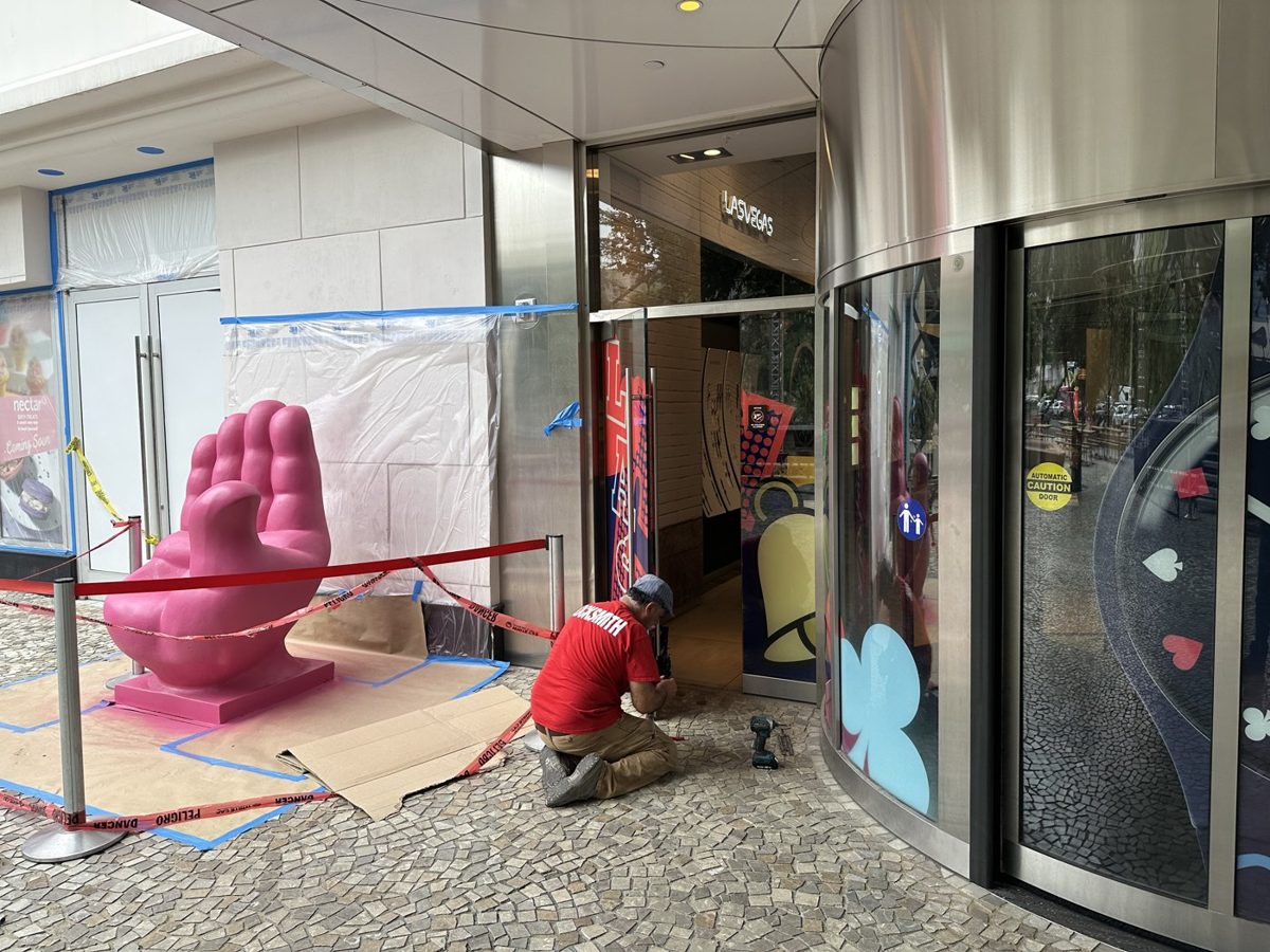 Locksmith in a marked red shirt repairing a storefront door with tools laid out on the ground