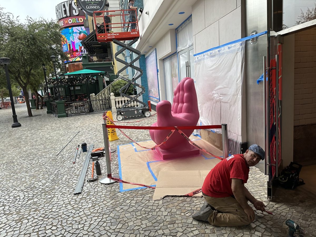Locksmith kneels on a cobblestone sidewalk outside a taped off Las Vegas Strip storefront with tools and door hardware laid out